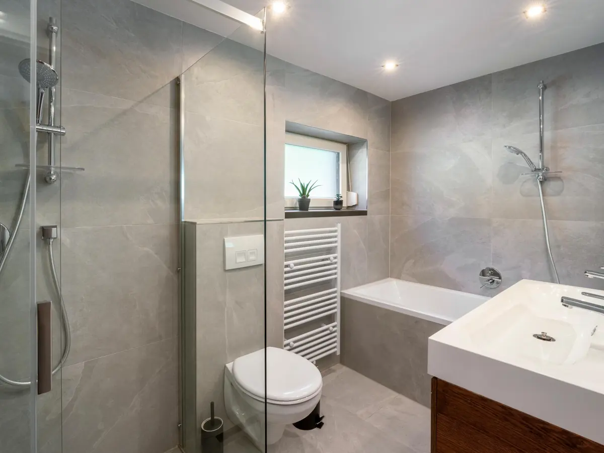 Ein Bad mit grauen Fliesen, begehbarer Dusche, Badewanne und Waschbecken.