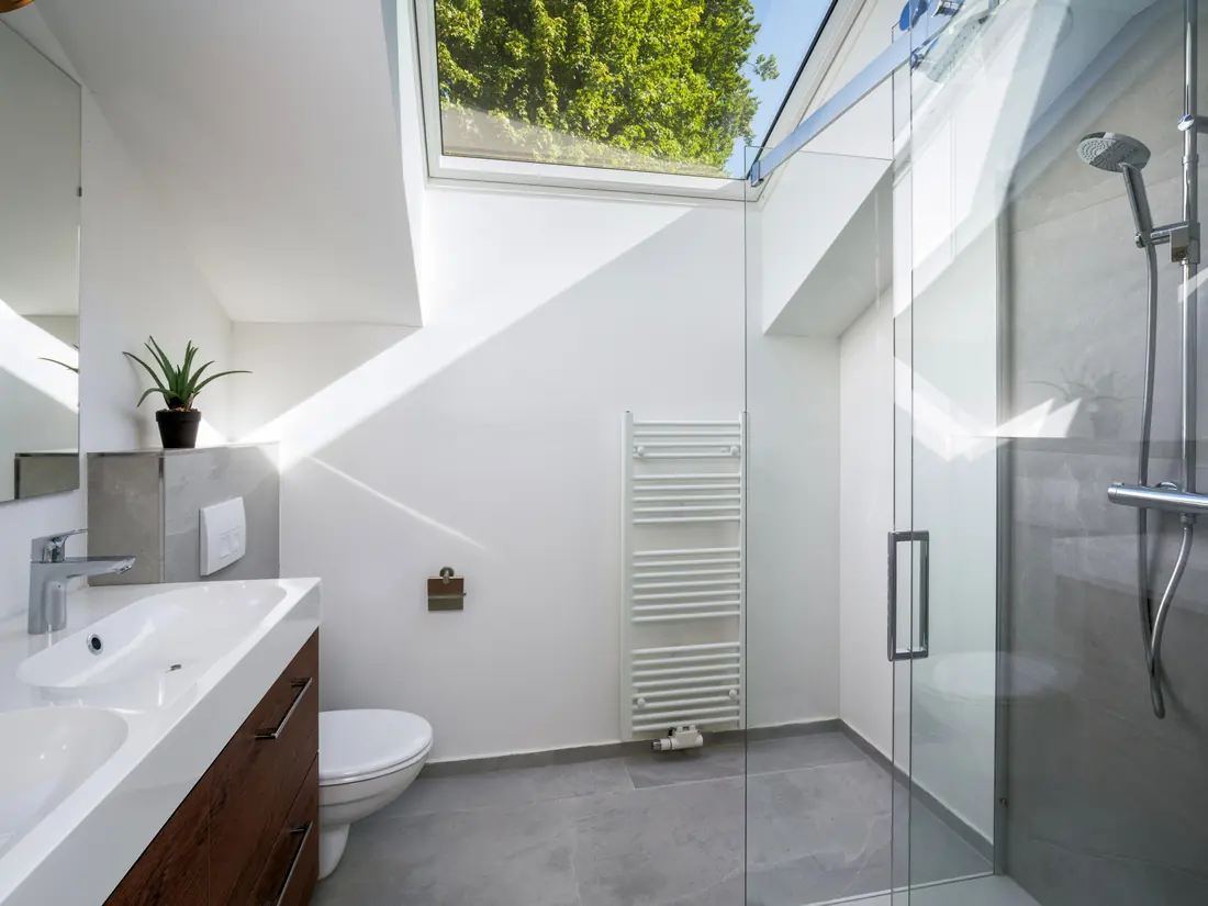 Een badkamer onder een groot dakraam met twee wastafels, een inloopdouche en een handdoekradiator.