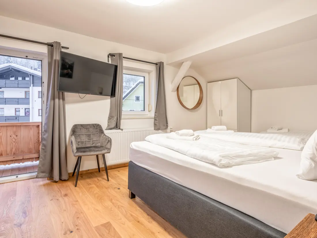 Een slaapkamer met een televisie aan de wand en een deur naar een houten balkon.