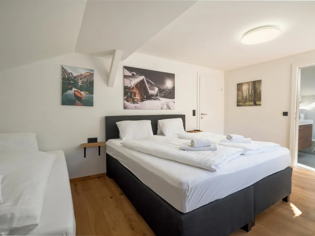 Een slaapkamer onder de schuine kap met een tweepersoonsbed en een eenpersoonsbed, en een deur naar de badkamer.