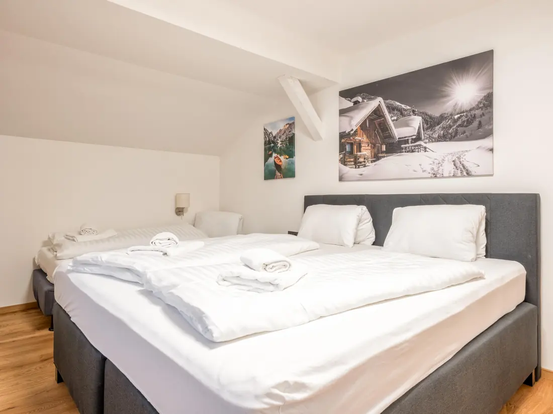 Een slaapkamer onder de schuine kap met een tweepersoonsbed, een eenpersoonsbed en een foto van een besneeuwde hut.