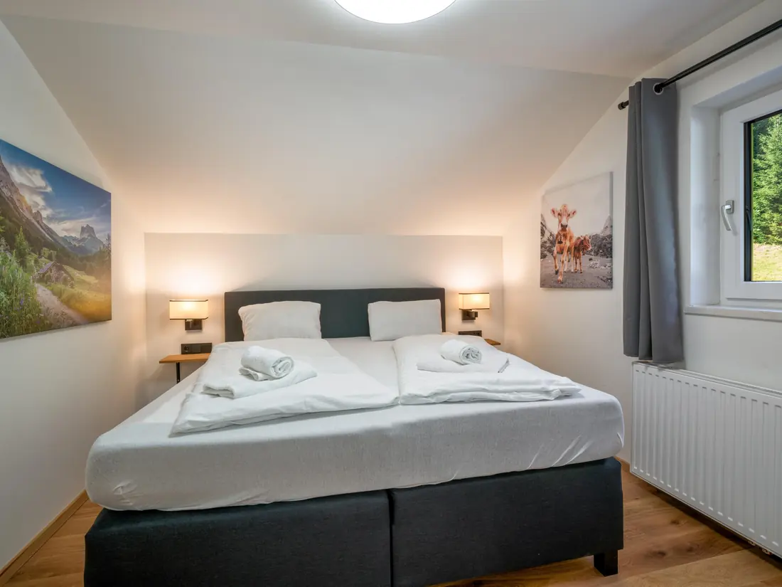 Een slaapkamer met een tweepersoonsbed, leeslampjes en uitzicht op het bos.