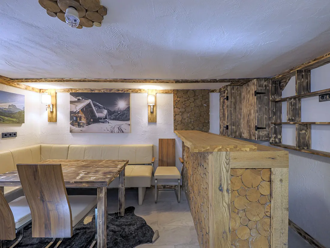 De kelderbar met een toog bekleed met houtschijven, een zithoek met bank en een houten tafel.