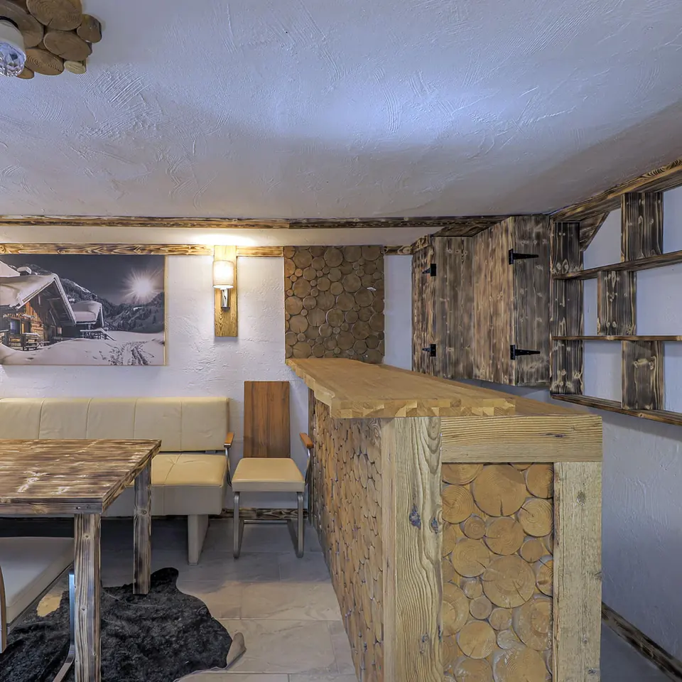 Der Kellerraum mit einer mit Baumscheiben verkleideten Bar, einer Sitzbank und einem Holztisch.