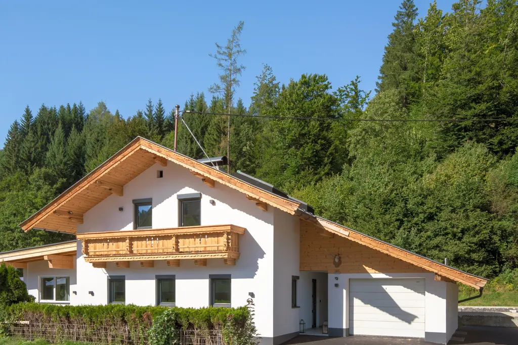 Hetzelfde chalet in de zomer, met een groen bos erachter en een heg langs de oprit.