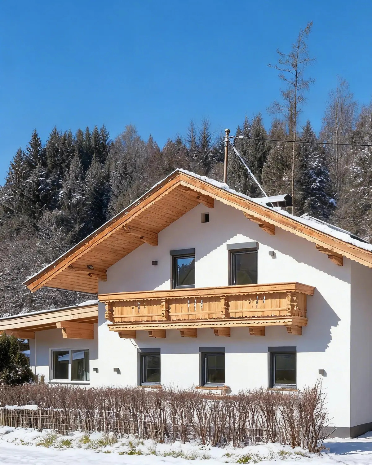 Chalet Hornblick with snow on the roof: a white house with a timber gable and a carved wooden balcony, in front of a snowy forest.