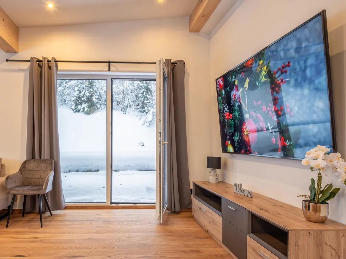 Een zithoek met een televisie aan de wand en een deur naar de besneeuwde tuin.