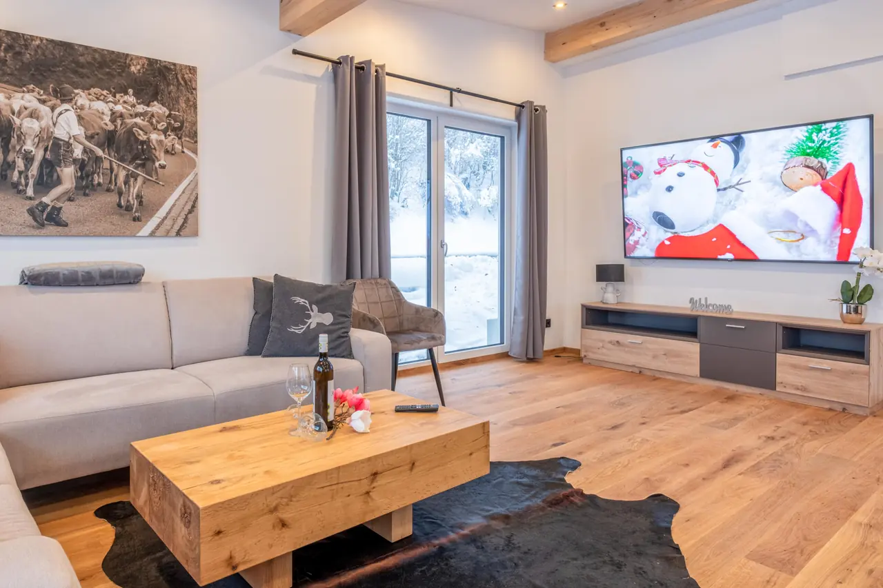 De zithoek met bank, salontafel en televisie, en sneeuw achter de terrasdeur.